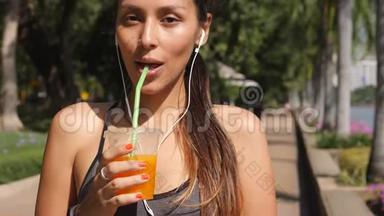 城市公园“微笑快<strong>乐跑</strong>者女孩在健身后喝新鲜橙汁”的肖像。 4K，慢动作。 泰国。